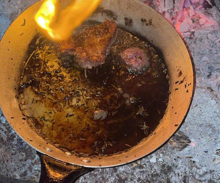 Goat meat sizzling in a pan over the fire.