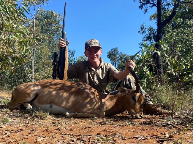Boy posing with rifle and trophy game