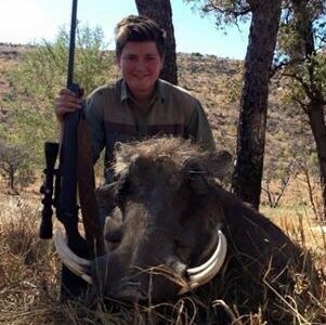 Teenage boy with his gun, posing with a warthog he shot.